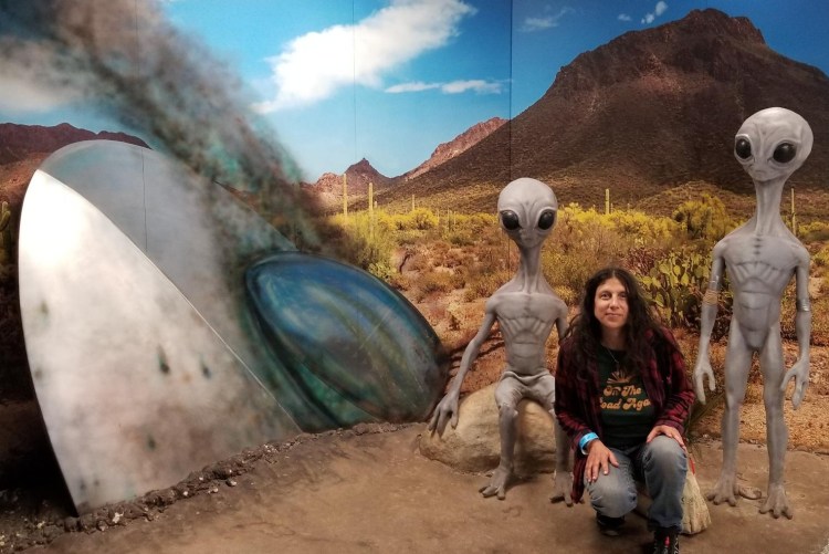 Lydia kneeling next to aliens and a crashed UFO