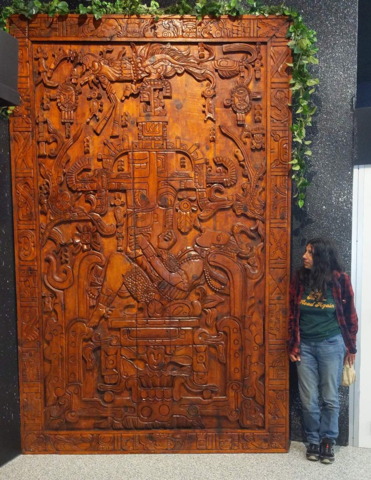 Lydia standing next to a replica of a wooden door that depicts an ancient astronaut.