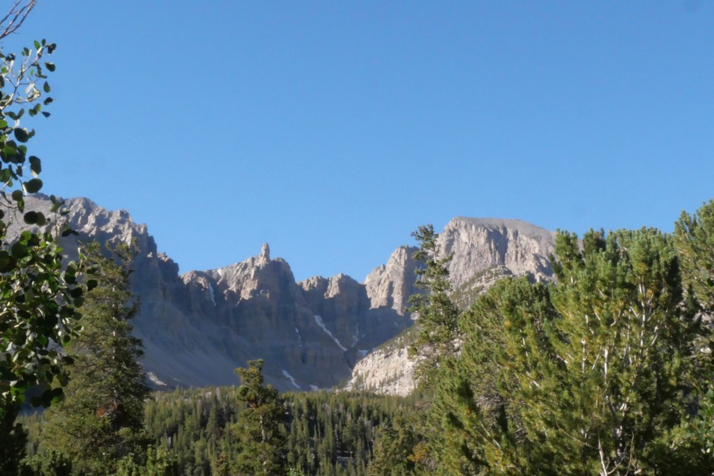 mountains with snow patches and tress in foreground