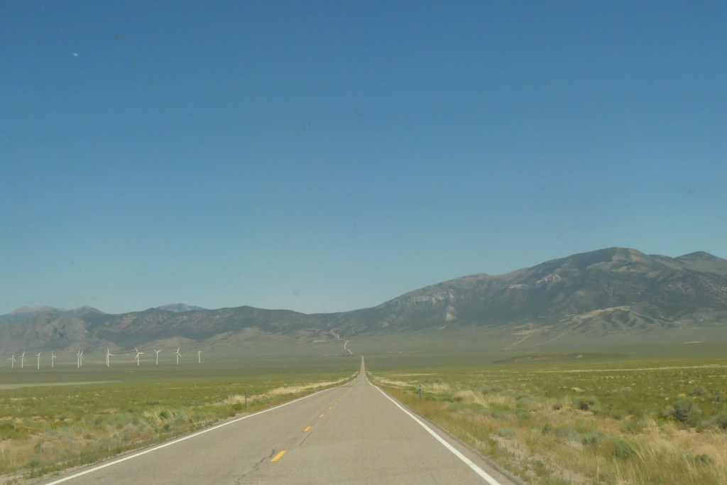straight two lane road with windmills and mountains in background